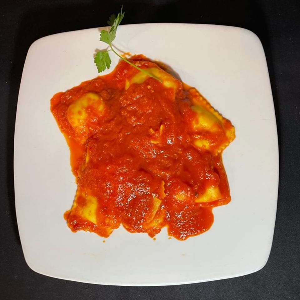 Ravioli pasta covered in red tomato sauce, garnished with a sprig of parsley on a white plate.