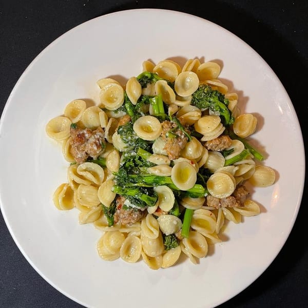Orecchiette pasta with broccoli rabe and sausage on a white plate.
