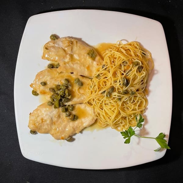 Chicken piccata with capers and lemon sauce, served with a side of spaghetti on a white plate.