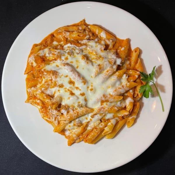 Penne pasta with meat sauce and melted mozzarella cheese, garnished with parsley on a white plate.