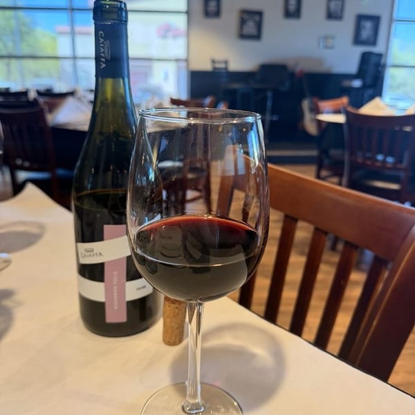 A glass of red wine and a bottle of Caiassa wine on a white tablecloth in a restaurant.