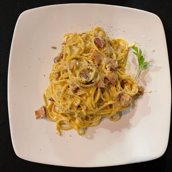 Creamy carbonara pasta with bacon bits, black pepper, and a parsley garnish on a white plate.